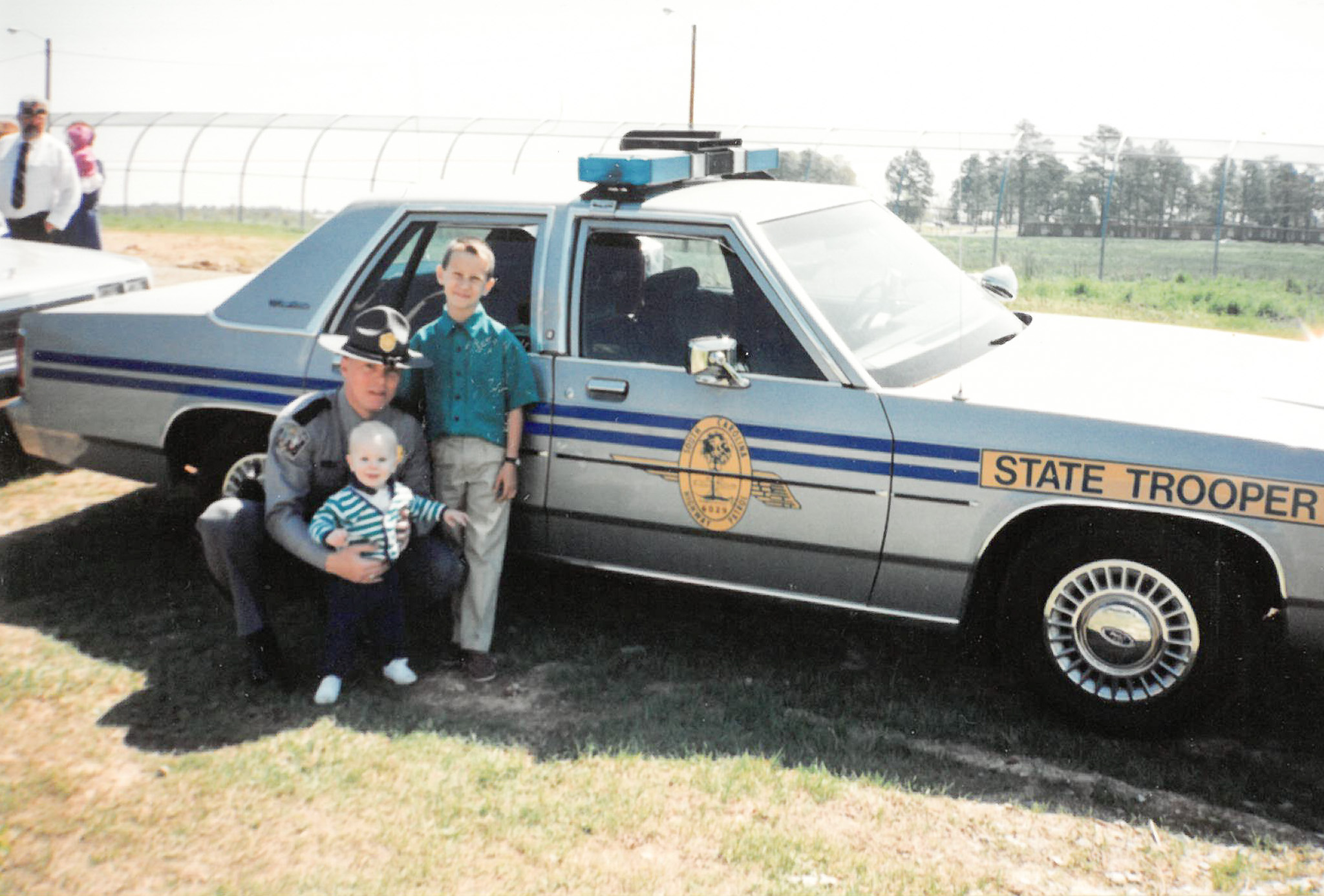 Trooper Albert with kids in front of a Highway Patrol car
